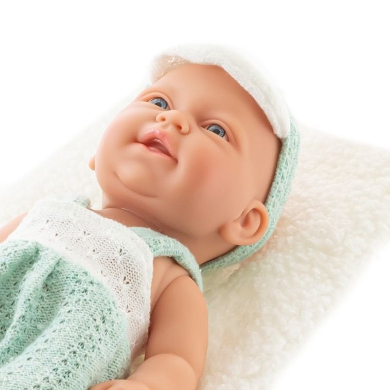 Lalka niemowlę w zielonym ubranku leży na białej miękkiej poduszce – zbliżenie twarzy
