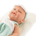 Lalka niemowlę w zielonym ubranku leży na białej miękkiej poduszce – zbliżenie twarzy
